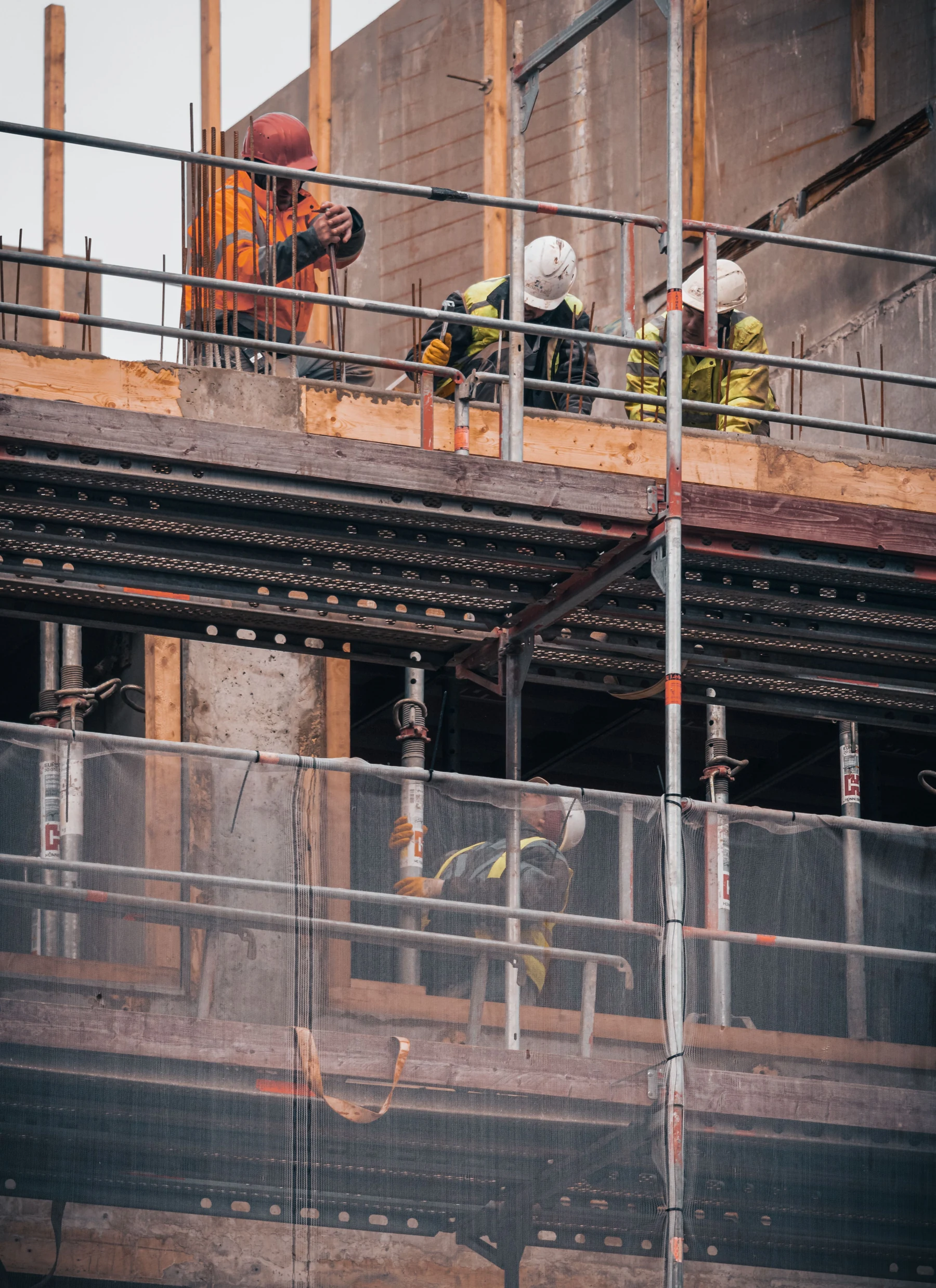 Bauarbeiter in benutzter Arbeitskleidung arbeiten hinter einem Gerüst an der Schalung eines Rohbaus in Hamburg.